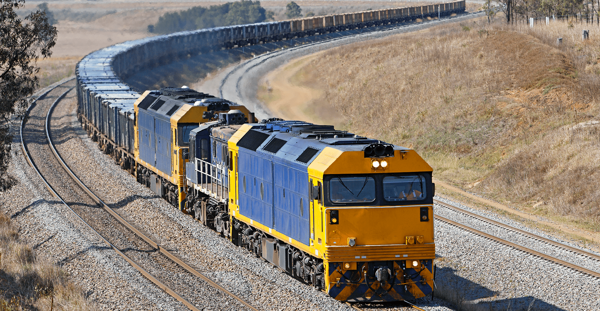 A train moving swiftly along the tracks, surrounded by greenery and a clear blue sky.