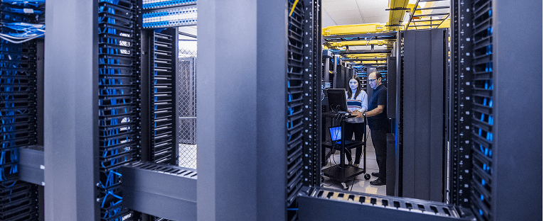 A man is positioned in a large server room, surrounded by numerous servers and equipment.