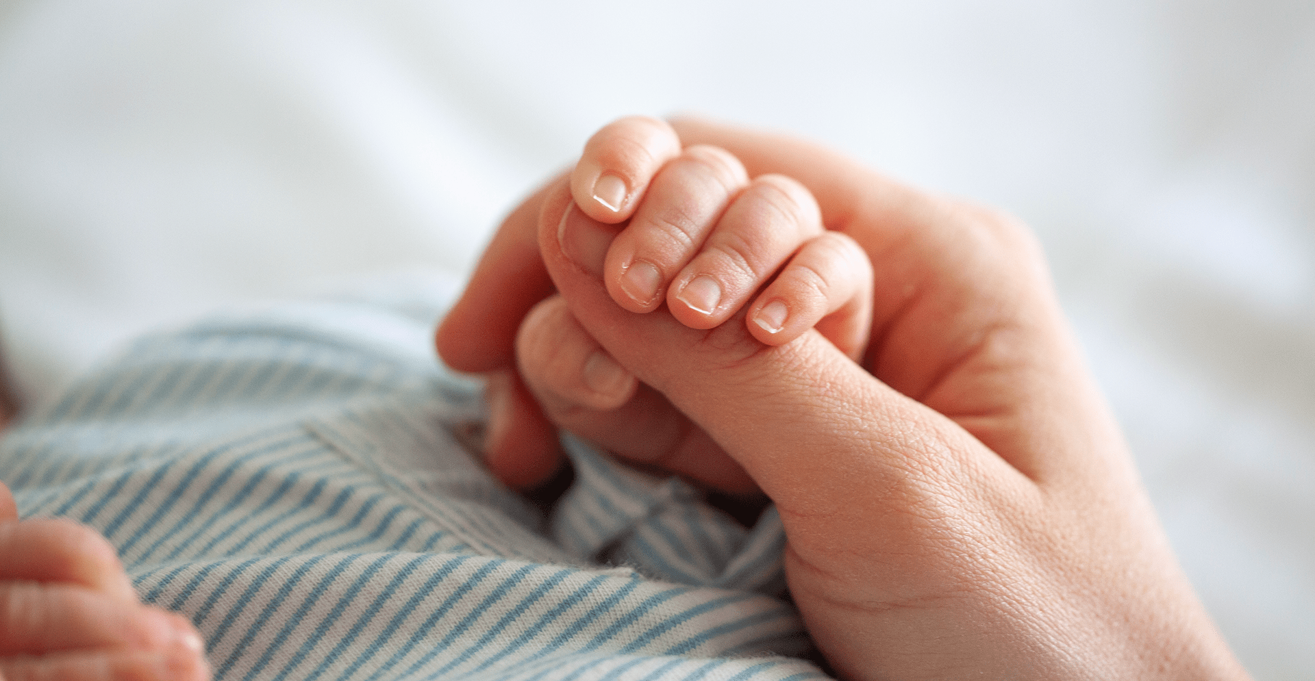 A close-up of an adult's hand clasping a baby's tiny fingers, symbolizing love and care.