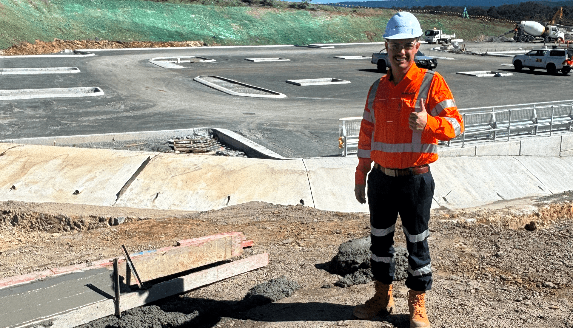 A man wearing an orange safety vest stands next to a construction site.