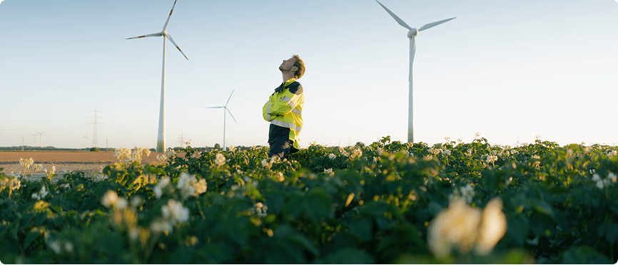 A person is seen in a field filled with green plants, enjoying the natural landscape under bright daylight.