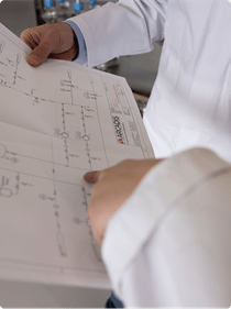 A man in a lab coat is holding a blueprint, indicating his involvement in research or design work.