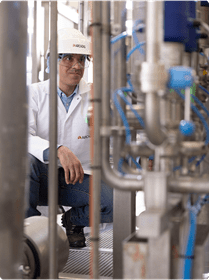  A man wearing a white lab coat sits on a bench, looking contemplative in a professional setting.