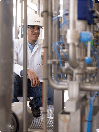  A man wearing a white lab coat sits on a bench, looking contemplative in a professional setting.