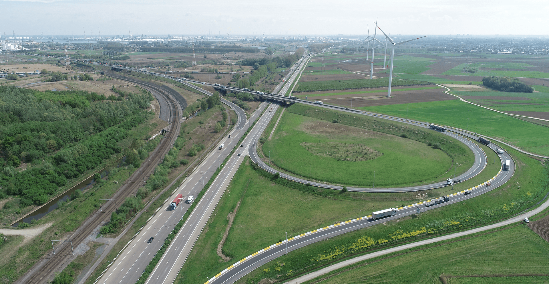 Aerial view of a highway surrounded by several wind turbines, showcasing renewable energy alongside transportation infrastructure.