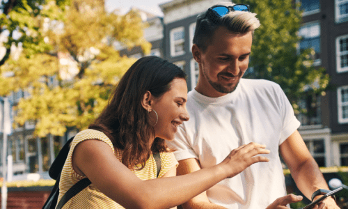 A man and woman stand beside bicycles, intently examining a tablet together in an outdoor setting.