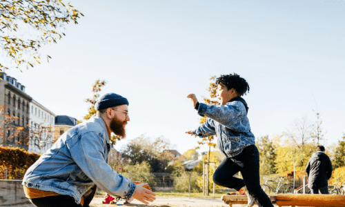 A man and boy joyfully playing together in a vibrant park, surrounded by greenery and sunshine.