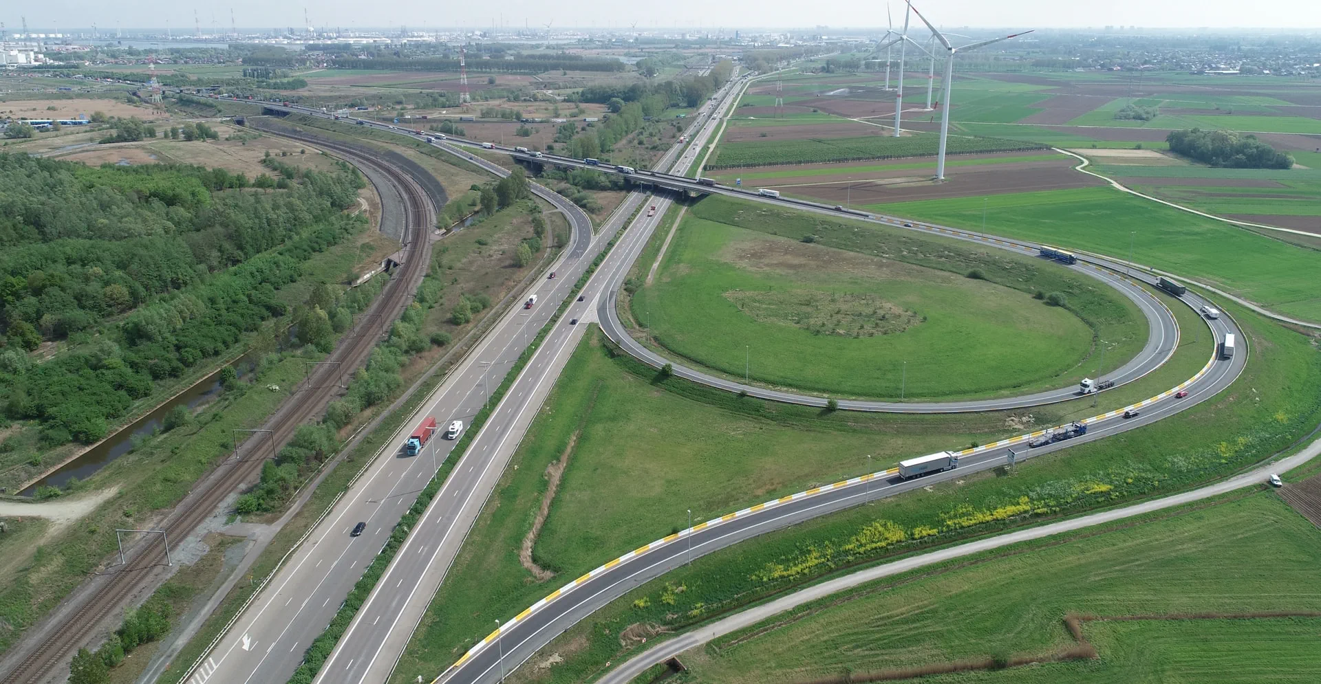Aerial view of a highway featuring a railroad and several wind turbines in the surrounding landscape.