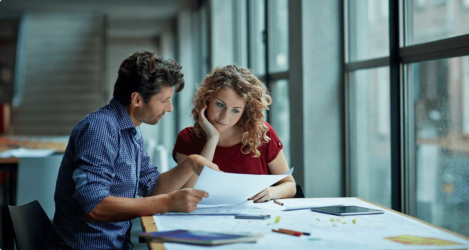 A man and woman at a table, examining papers intently, suggesting a collaborative discussion.